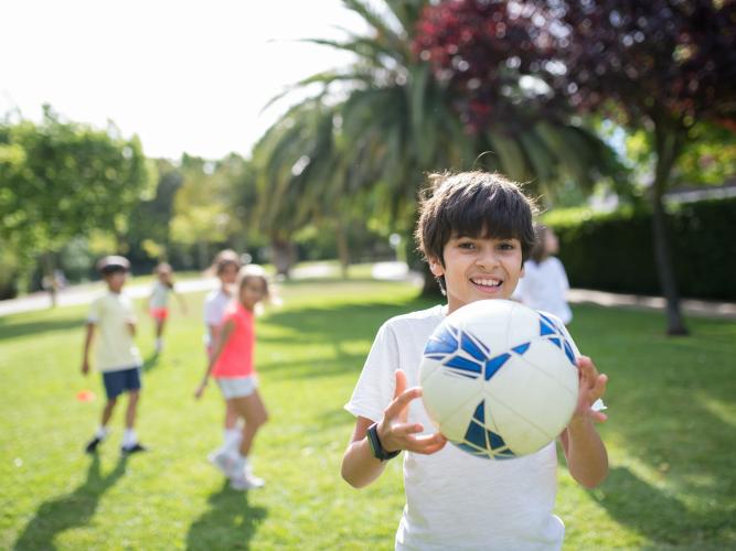 Image of boy holding an football with other children visible in the background 