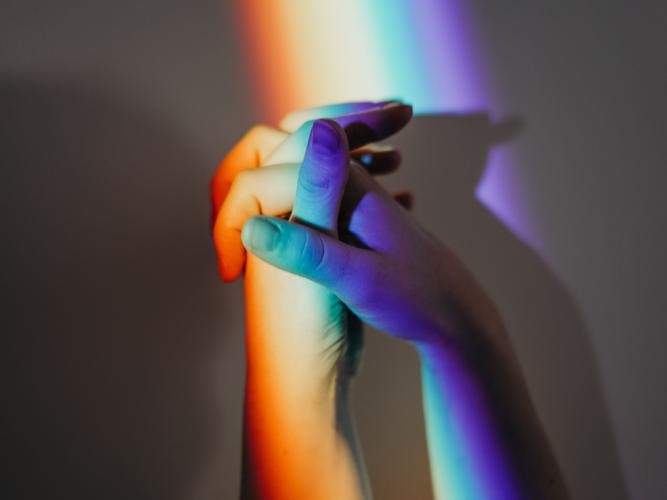 Close-up image of two hands in rainbow coloured light