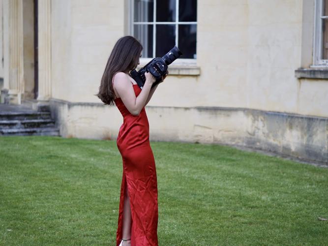 Sarah Brand stands outside holding a camera on the set of her music video