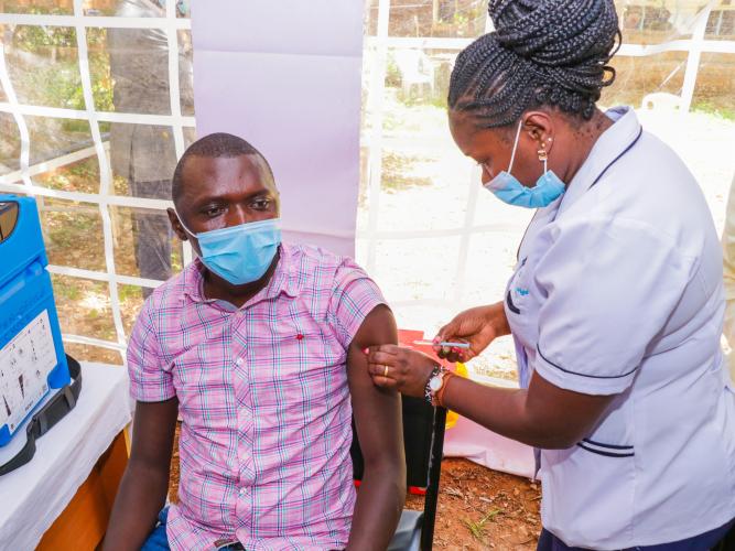 A female nurse gives a man an injection at an outdoor hospital