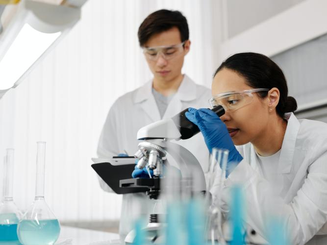 Male and female scientists look at a microscope 