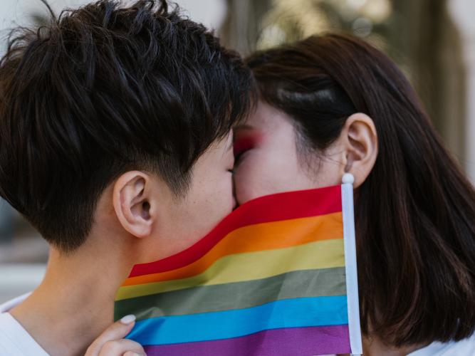 Two women kiss behind a LGBTQ+ pride flag