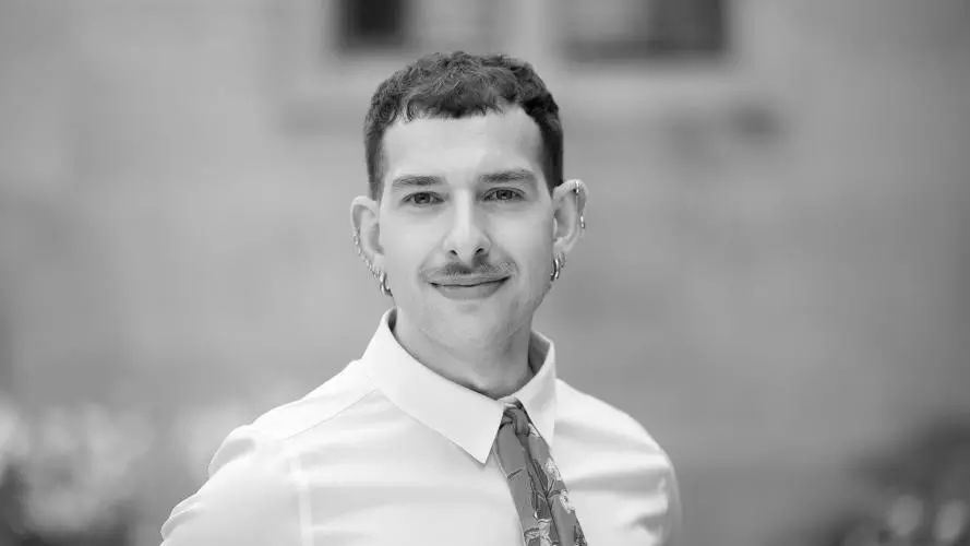 Martin has short dark hair. He is wearing a white shirt with a patterned tie and several small earrings.