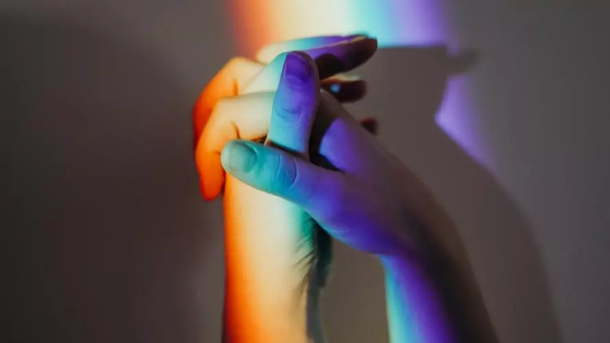 Close-up image of two hands in rainbow coloured light