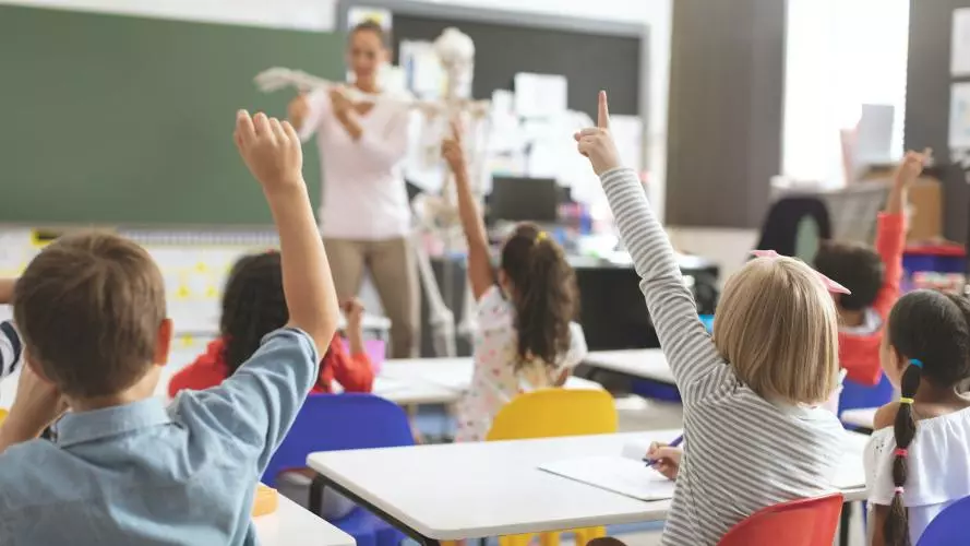 Young children raising their hands in a school classroom