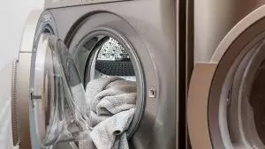 Silver washing machine with towels hanging out of door.