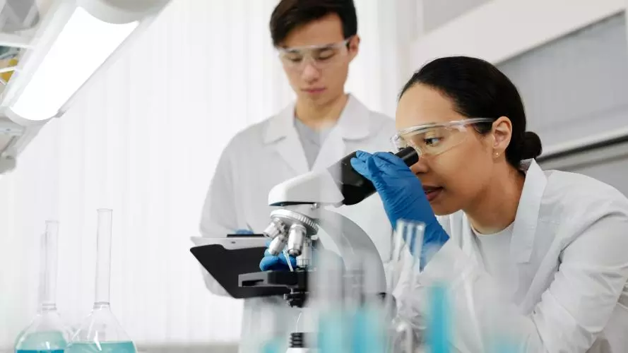 Male and female scientists look at a microscope 