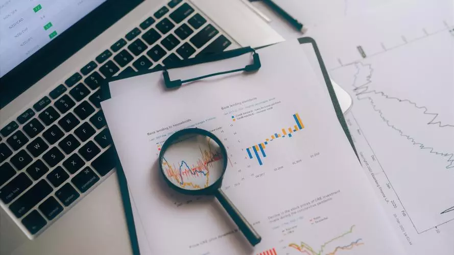 A magnifying glass resting on top of graphs and a laptop