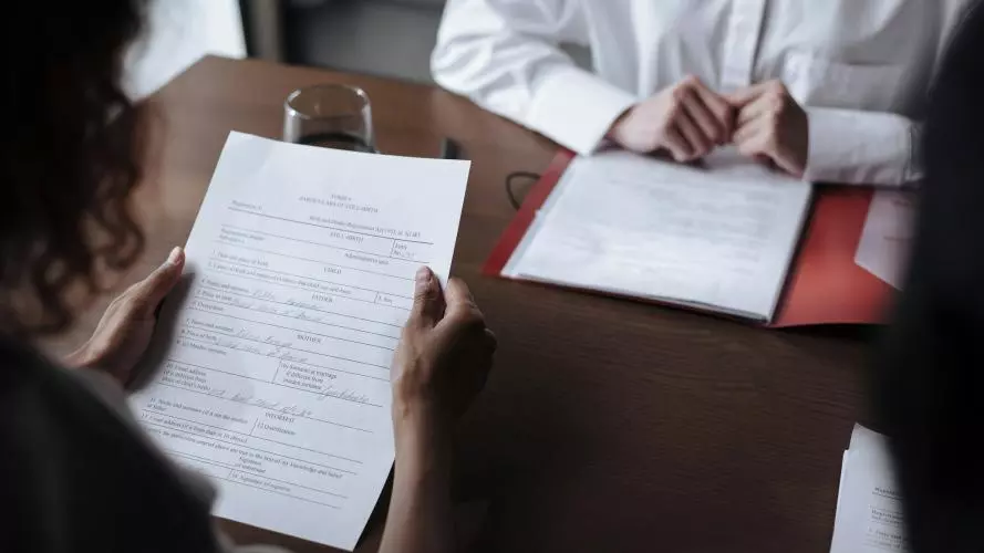 Two people sit opposite each other at a desk, reading documents