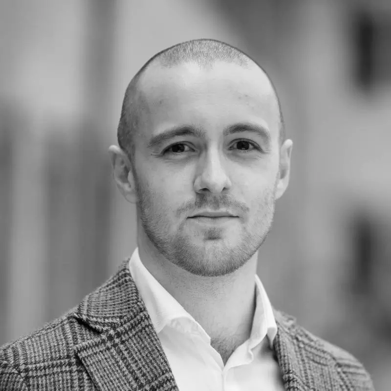 Hloedver has shaved hair and is wearing a checked blazer and white shirt