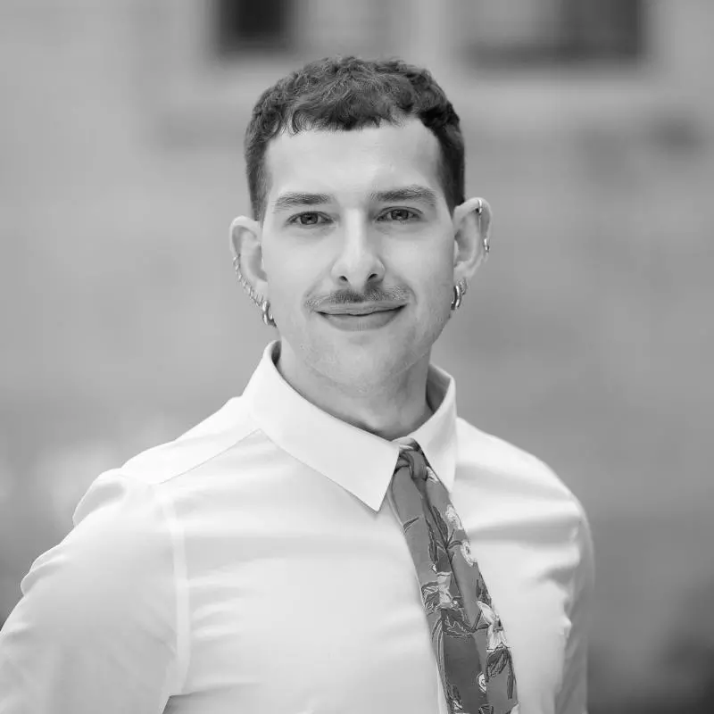 Martin has short dark hair. He is wearing a white shirt with a patterned tie and several small earrings.