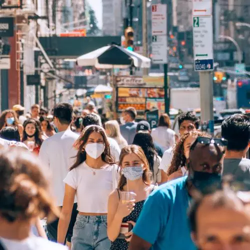 People walk along a crowded street, wearing masks