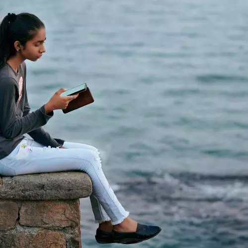 Image of a young woman sitting near the sea using a mobile phone