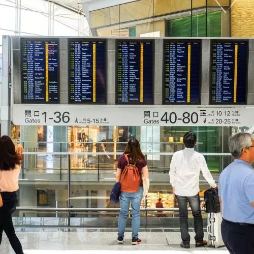 People look at a flight departure board in Hong Kong International Airport