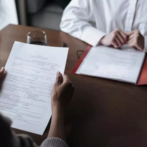 Two people sit opposite each other at a desk, reading documents