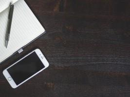 Lined notepad and pen next to iPhone