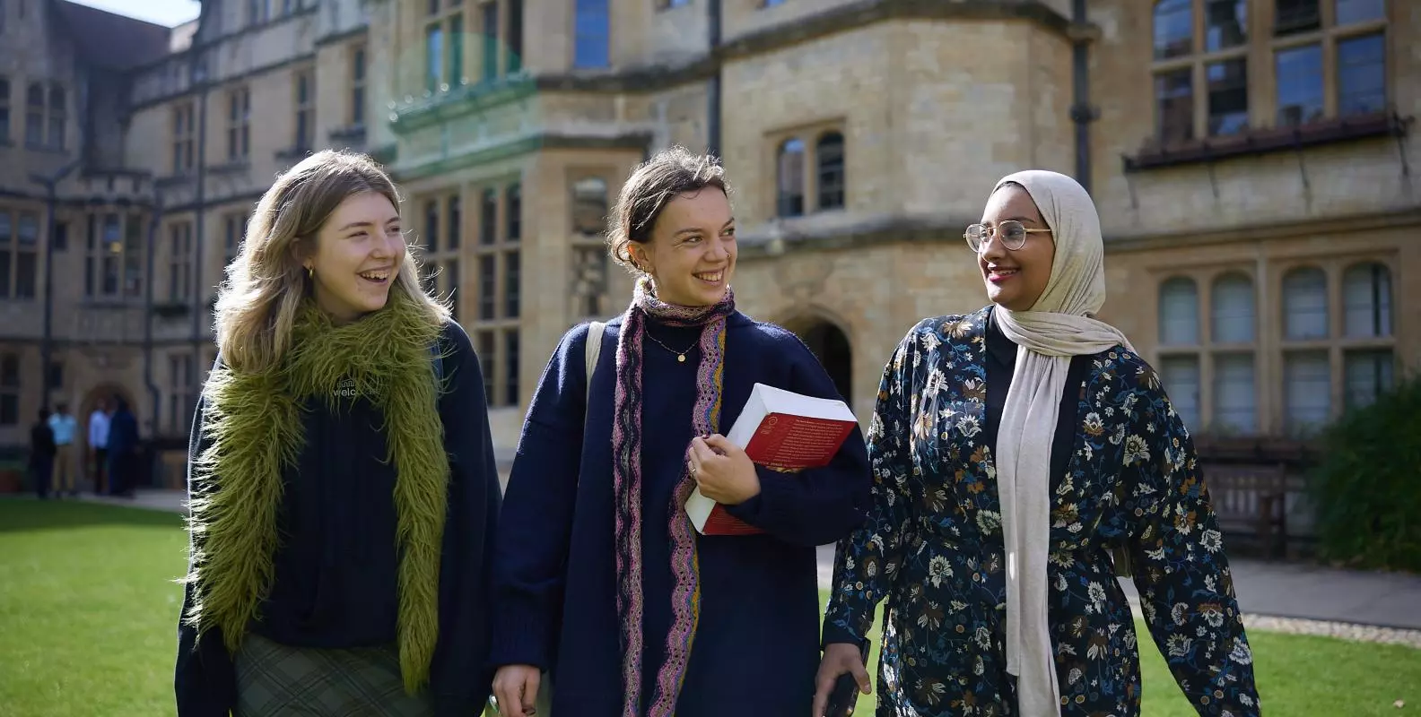 Three students walk across a college lawn in Autumn