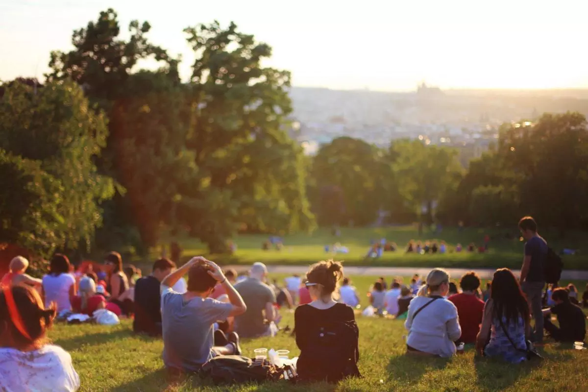A crowd of people sit on a grassy hill in the sunshine